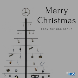 Minimalistischer Weihnachtsgruß mit einer Metallkonstruktion in Form eines Weihnachtsbaums, dekoriert mit kleinen silbernen und goldenen Anhängern und gekrönt von einem Mercedes-Stern, dazu der Text "Merry Christmas from the HDO Group" auf grauem Hintergrund.