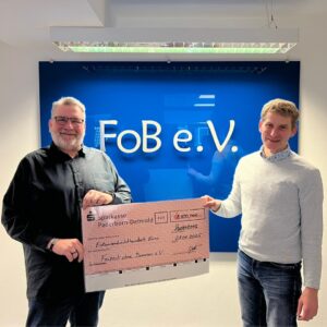 Zwei Männer stehen vor einem blauen Schild mit der Aufschrift 'FoB e.V.' und halten gemeinsam einen großen roten Spendenscheck über 1800 Euro von der Sparkasse Paderborn-Detmold, datiert auf den 21.01.2025.