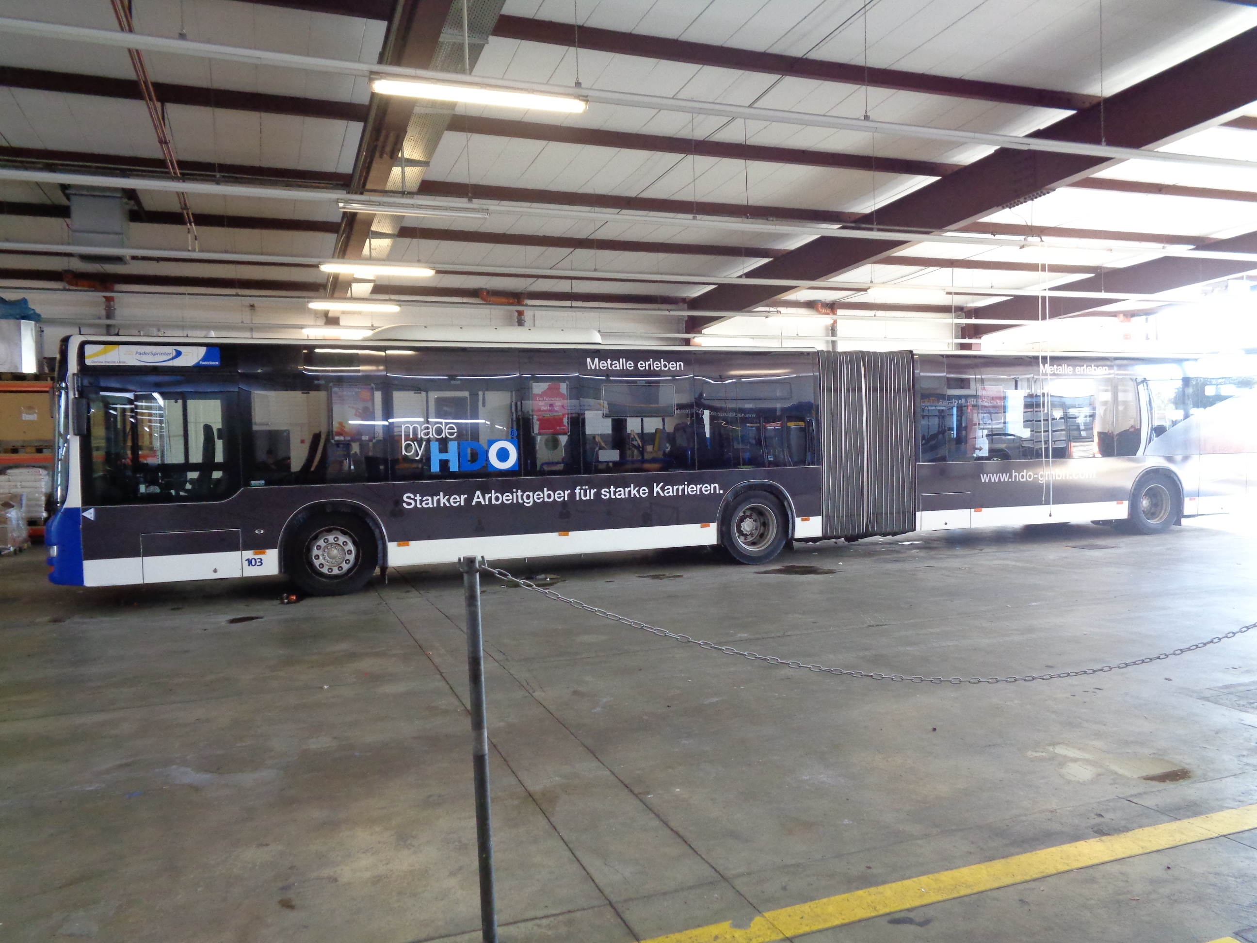 Schwarz-weißer Gelenkbus in einer Halle mit der Aufschrift „made by HDO“ in Blau und Weiß, dazu der Slogan „Starker Arbeitgeber für starke Karrieren.“ auf der Seite