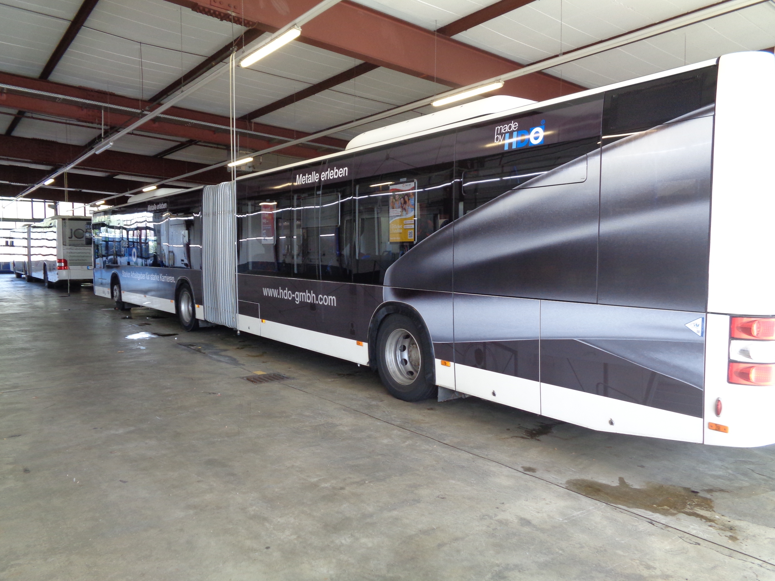 Großer Gelenkbus in einer Halle mit Beklebung, die den Schriftzug 'made by HDO' und die Webseite 'www.hdo-gmbh.com' zeigt.