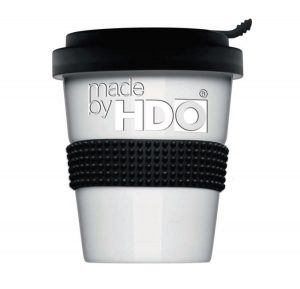 Weißer Coffee-to-go-Becher mit schwarzem Deckel und schwarzem Noppenband in der Mitte, auf dem Becher steht geprägt und hervorgehoben der Schriftzug "made by HDO"