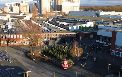 Blick auf ein Fabrikgelände mit mehreren Gebäuden, Solarzellen auf Dächern und einem aufblasbaren Weihnachtsmann im Hof.