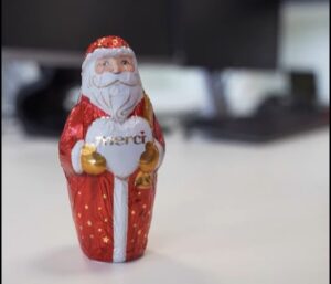 Schokoladenfigur von Weihnachtsmann in rotem Gewand und weißem Bart, hält ein Herz mit dem Schriftzug "merci"