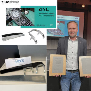 Mann in Sakko und Jeans hält zwei Holzrahmen mit Urkunden, im Hintergrund eine Projektionswand mit einer Präsentation zur ZINC Diecasting-Auszeichnung 2022 und mehreren Metallteilen sowie einem Schild "made by HDO".