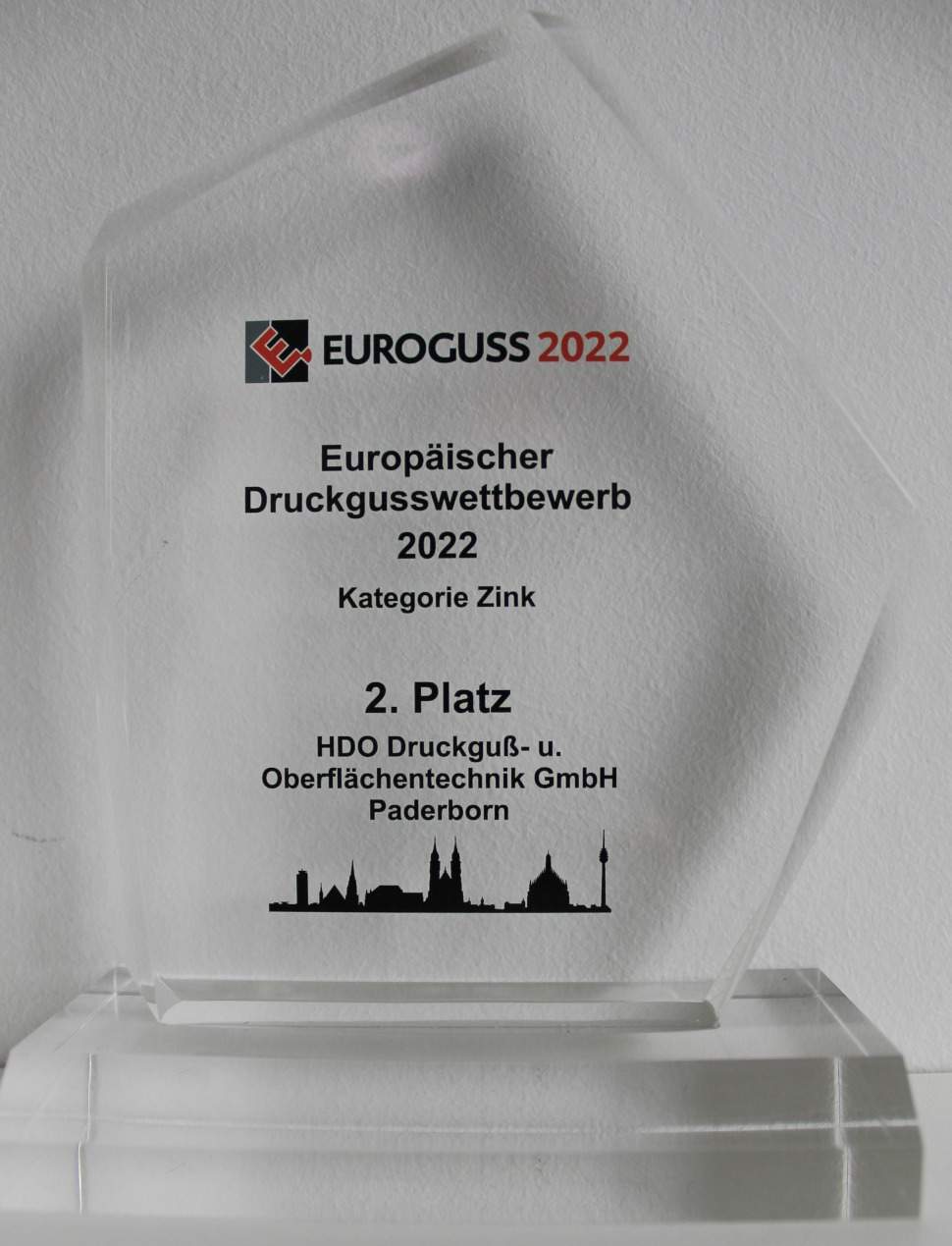 Glas-Trophäe für den 2. Platz beim Europäischen Druckgusswettbewerb 2022 in der Kategorie Zink, verliehen an HDO Druckguß- und Oberflächentechnik GmbH Paderborn, mit Euroguss 2022 Logo und Stadtsilhouette