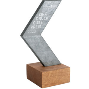 Auszeichnung Zink Druckguss Preis 2020, dreieckige Metallskulptur auf Holzsockel mit eingelassener Schrift, ergänzt um das Logo HDO dezent integriert