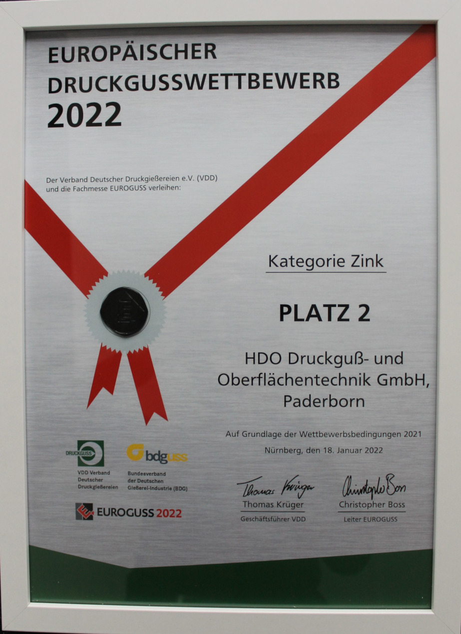 Urkunde für den Europäischen Druckgusswettbewerb 2022 mit rotem Band und Siegel, vergeben an HDO Druckguß- und Oberflächentechnik GmbH, Paderborn, für Platz 2 in der Kategorie Zink, unterzeichnet von Thomas Krüger und Christopher Boss, mit Logos von VDD Verband Deutscher Druckgießereien, BDG Bundesverband der Deutschen Gießerei-Industrie und Euroguss 2022.