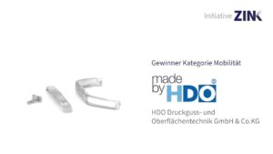 Drei kleine silberne Metallteile neben dem Text "Gewinner Kategorie Mobilität made by HDO HDO Druckguss- und Oberflächentechnik GmbH & Co.KG" und dem Logo von Initiative ZINK in der oberen rechten Ecke.